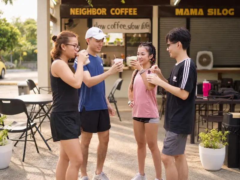 Friends in workout clothes sharing drinks outside Neighbor Coffee and Mama Silog