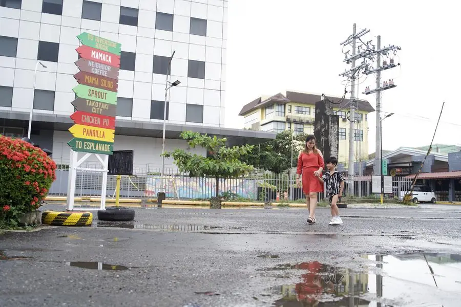 A mother and child walking past the colorful signpost pointing to Mamaca, Sprout, Mama Silog and Panrilla